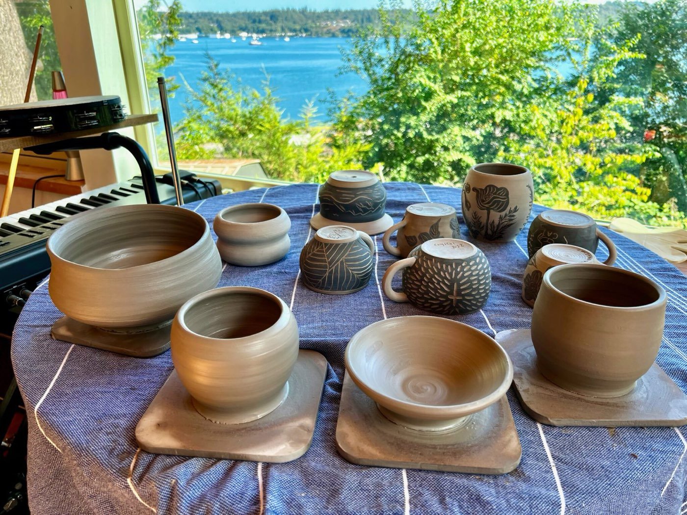 Handmade stoneware mugs and bowls with carved designs on a table by the water